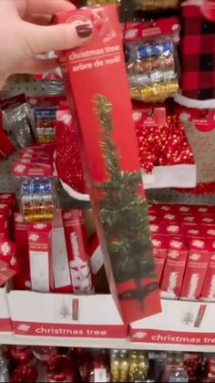 a person is holding up a christmas tree in a store aisle with red and white boxes