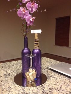 two wine bottles with flowers in them sitting on a marble counter top next to a laptop