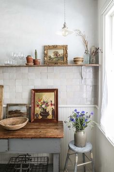 a room with a table, potted plants and pictures on the wall above it