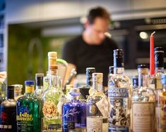 many different types of liquor bottles on a bar counter with a man in the background