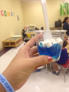 a hand holding a cup with marshmallows in it and people sitting around