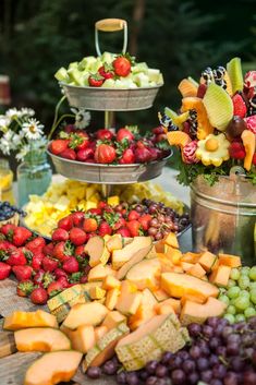 an assortment of fruits and cheeses on display in metal buckets at a buffet table