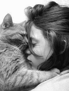 a woman laying in bed with her head on the back of a cat's neck