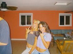 two women standing in a living room smiling and making the peace sign with their hands