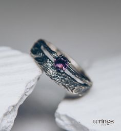 two wedding rings sitting on top of a piece of white wood with a purple stone in the center