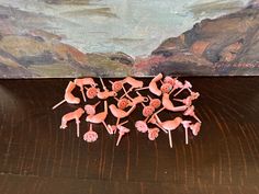 a group of pink figurines sitting on top of a wooden table next to a painting