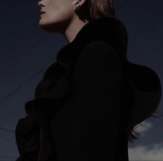 a woman with her head tilted to the side, wearing earrings and a black coat