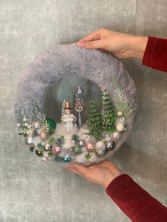 two hands holding a christmas wreath made out of fake snowmen and fir trees with ornaments on it