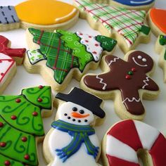 many decorated cookies are displayed on a white tablecloth with christmas trees and snowmen