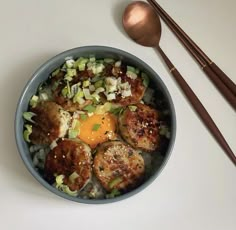 a bowl filled with meat and vegetables next to chopsticks on a white surface