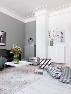 a living room filled with furniture and flowers on top of a white table in front of a gray wall