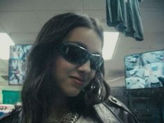 a woman wearing sunglasses talking on her cell phone in a room with televisions behind her