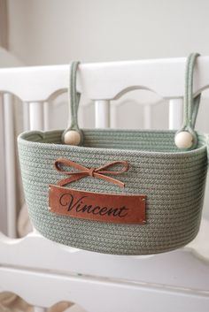 a basket hanging from the side of a crib with a name tag on it