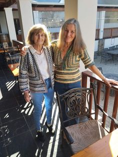 two women standing next to each other in front of a balcony with tables and chairs