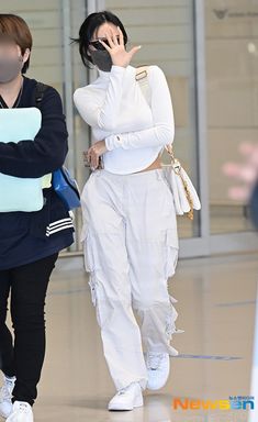 two women in white outfits are walking through an airport terminal, one is talking on the phone