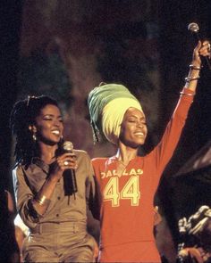 two women singing into microphones while one holds her hand up in the air and smiles