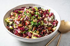 a white bowl filled with salad next to two gold spoons on top of a table