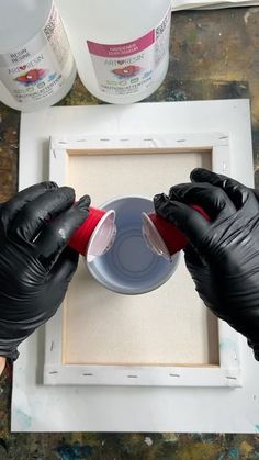 two hands in black gloves are pouring something into a container with red liquid on it