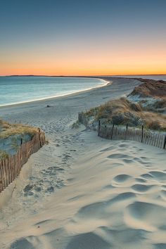 the sun is setting at the beach with sand dunes and fenced in area on either side