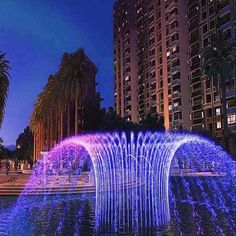 an illuminated fountain in front of tall buildings