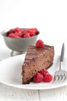 a piece of chocolate cheesecake with raspberries on a plate next to a fork