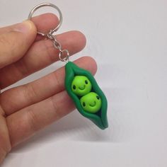 two peas in a pod shaped keychain being held by someone's hand