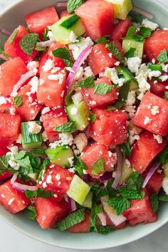 watermelon salad with feta cheese, onions and cucumbers in a white bowl