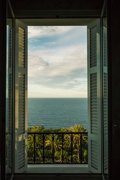 an open window looking out at the ocean and palm trees in front of it with white shutters