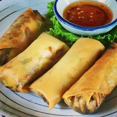 three spring rolls on a plate with dipping sauce