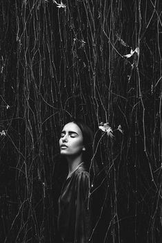 a black and white photo of a woman's face in front of vines on the wall