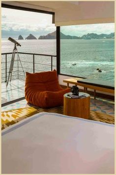 Plush orange armchair by a window overlooking a serene sea with distant islands, complemented by a cozy interior with a telescope. Ocean Views