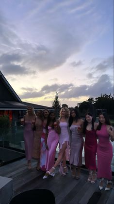 a group of women standing next to each other on a wooden deck near water at sunset