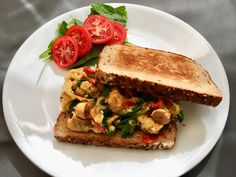 a white plate topped with a cut in half sandwich next to tomatoes and lettuce