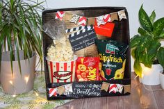 a box filled with popcorn and snacks on top of a table next to potted plants