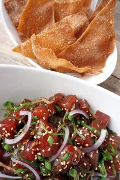 a white bowl filled with food next to some tortilla chips on top of a wooden table