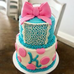 a three tiered cake with blue and pink frosting, decorated with a large bow