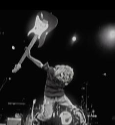 black and white photograph of a person playing guitar on stage with lights in the background