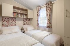 two beds in a small room with curtains on the windowsill and shelves above them