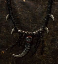 Embrace a touch of mystique with the Shaman Necklace, a captivating piece that bridges the realms of fantasy and post-apocalyptic worlds. Crafted intricately with plastic goat horn accented with faux bones, this neck jewelry embodies the essence of shamanic artistry. Whether you're preparing for a ConQuest of Mythodea event, seeking a unique horror lover gift, or enhancing a shaman costume for Halloween, this necklace adorned with icks and claws will add an intriguing edge to your ensemble. Elev Adjustable Fantasy Necklaces For Fantasy Events, Adjustable Fantasy Necklace For Fantasy Events, Handmade Medieval Necklaces For Larp, Medieval Black Jewelry For Larp, Unique Handmade Necklaces For Cosplay, Unique Handmade Necklace For Cosplay, Adjustable Fantasy Necklaces For Cosplay, Gothic Hand-cast Halloween Necklaces, Adjustable Fantasy Necklace For Cosplay