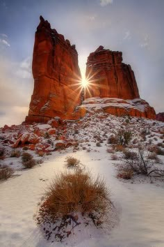 the sun shines brightly in front of red rock formations on a snowy mountaintop