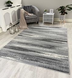 a gray and white rug in a living room next to a grey chair with a plant on it