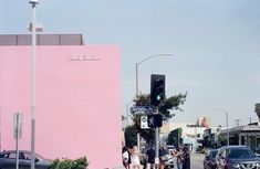 people are walking on the sidewalk in front of a pink building with a traffic light