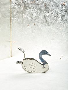 a metal duck sitting in the snow next to a white wall with peeling paint on it