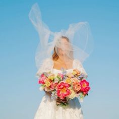 a woman in a wedding dress holding a bouquet of flowers with veil over her head