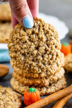 a hand picking up an oatmeal cookie with cinnamon sticks next to it