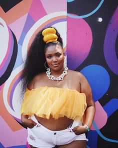 a woman standing in front of a colorful wall wearing a yellow top and white shorts