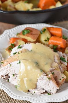 a white plate topped with meat covered in gravy next to potatoes and carrots