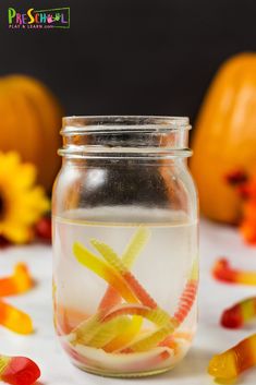 a jar filled with jelly worms and candy corn on top of a table next to sunflowers