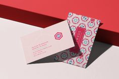 two folded business cards sitting next to each other on top of a white table with red and blue designs