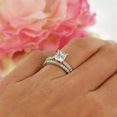 a woman's hand with a diamond ring on it and a pink flower in the background